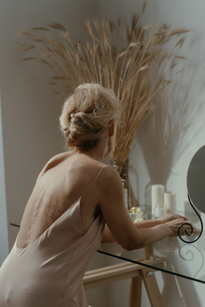 Graceful woman in sleepwear leans on glass table with candles, creating a serene indoor ambiance.