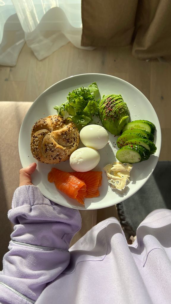 Plate of healthy breakfast including smoked salmon, eggs, and avocado held by a person indoors.